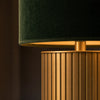 Detail of the Albany lamp — close-up of the brushed brass fluted column and the rolled bottom edge of the deep forest-green velvet drum shade, warm directional light catching the brass flutes and the soft pile of the velvet