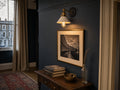 Bayswater white-cone-and-brass-collar wall sconce with Edison bulb mounted on a Hague Blue Edwardian hallway wall above a framed black-and-white photograph of a Bayswater crescent, antique walnut console table with stacked hardback books and brass keys in a small bronze bowl, Persian runner on oak floor, sash window onto stuccoed terrace at golden hour