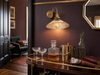 Belgravia amber-fluted-glass coolie-hat wall sconce in polished brass mounted on a deep aubergine Brinjal plaster wall in a Belgravia townhouse drinks corner, above a walnut-and-polished-brass Art-Deco bar cart with crystal coupes, whisky decanter, and brass ice bucket