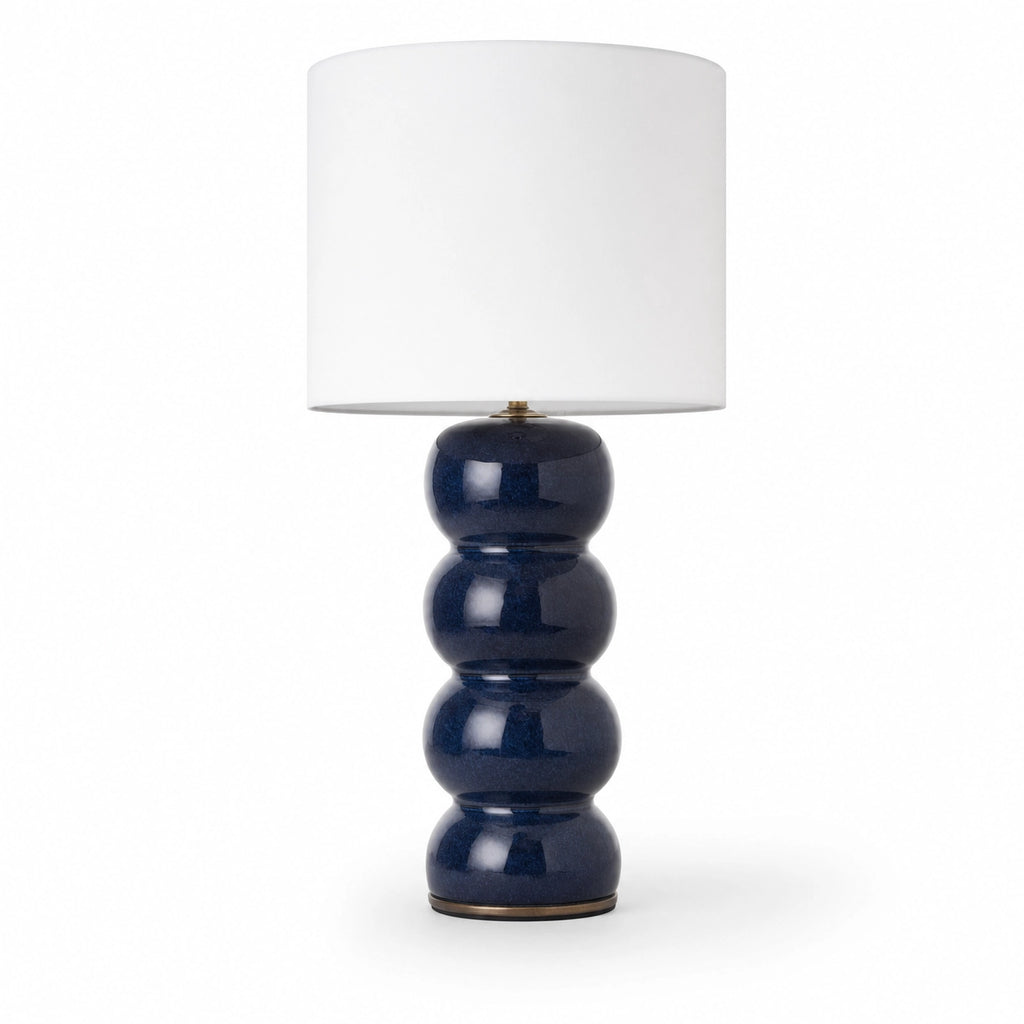 Cosmati bobbin ceramic table lamp on white background — stacked rounded ceramic forms in indigo high-gloss glaze beneath a crisp white drum shade