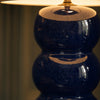 Detail of the Cosmati ceramic base — stacked bobbins in deep indigo high-gloss glaze, showing the bobbin form, brass collar, and warm reflected lamp light