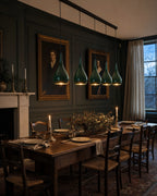 Halcombe five-light linear pendant in Studio Green suspended above a long walnut dining table in a forest-green panelled English dining room at dusk
