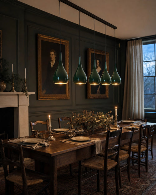 Halcombe five-light linear pendant in Studio Green suspended above a long walnut dining table in a forest-green panelled English dining room at dusk