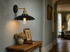 Marlow scalloped dome wall sconce in black metal with polished brass arm above an oak console table in an English country hotel hallway with duck-egg blue walls and oak parquet floor