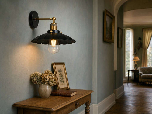 Marlow scalloped dome wall sconce in black metal with polished brass arm above an oak console table in an English country hotel hallway with duck-egg blue walls and oak parquet floor