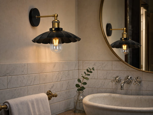 Marlow scalloped dome wall sconce above a marble basin in a boutique hotel bathroom with Carrara marble subway tiles and oval brass-framed mirror