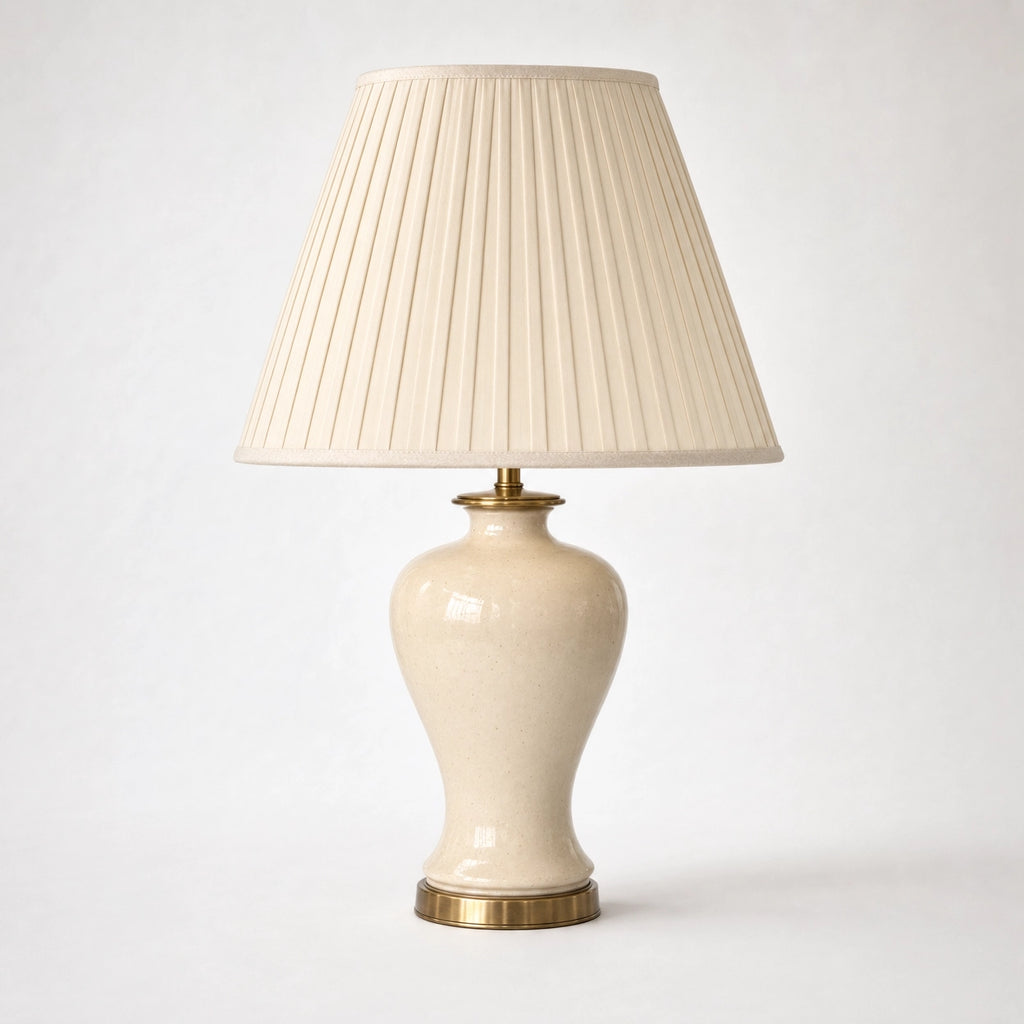 Salcombe table lamp on a soft warm-white background — full 56cm product view of the cream-glazed ceramic urn body on its antique-brass base plate beneath a tall classic empire-form shade in cream knife-pleated silk