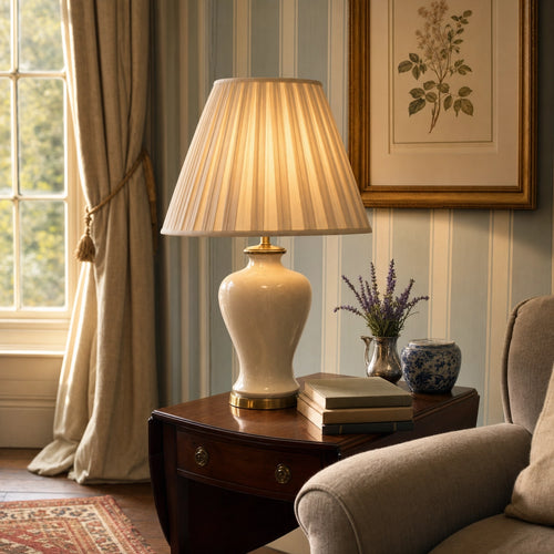 Salcombe cream ceramic urn lamp on a mahogany Pembroke side-table in a panelled English drawing room at golden hour, pleated cream silk shade pooling warm light against a duck-egg blue striped wall, gilt-framed botanical print, lavender in a silver vase and blue-and-white Chinese export porcelain