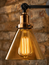 Close-up detail of the Shoreditch wall sconce showing amber glass cone shade and copper socket collar