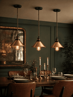 Three Wapping copper pendant lights hanging in a row above a dark wood dining table
